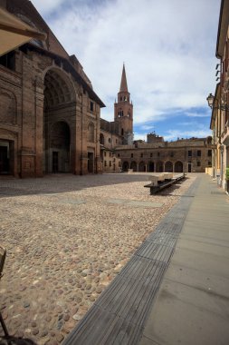 Mantova, İtalya - 27 Temmuz 2025 - Güneşli bir günde San Andrea Bazilikası 'nın bir tarafında çan kulesi ve bitişik binası ile kaldırımlı meydan