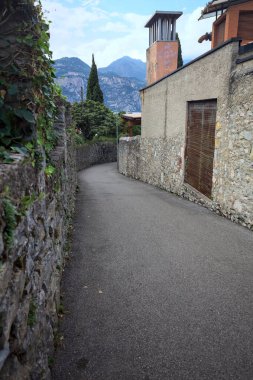 Taş bir duvarla çevrili dar bir sokak ve bir İtalyan köyünde bulutlu bir günde üzerinde çit büyüyen bir çit.