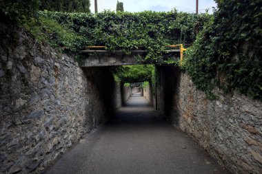 Bulutlu bir günde, İtalya 'nın bir köyünde ağaçlarla çevrili taştan duvarlarla çevrili taştan bir geçit.