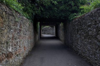 Bulutlu bir günde, İtalya 'nın bir köyünde ağaçlarla çevrili taştan duvarlarla çevrili taştan bir geçit.