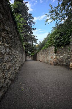 Bulutlu bir günde, İtalya 'nın bir köyünde ağaçlarla çevrili taştan duvarlarla çevrili taştan bir geçit.