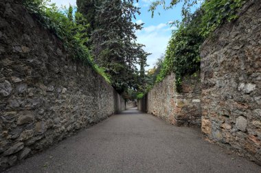 Bulutlu bir günde, İtalya 'nın bir köyünde ağaçlarla çevrili taştan duvarlarla çevrili taştan bir geçit.