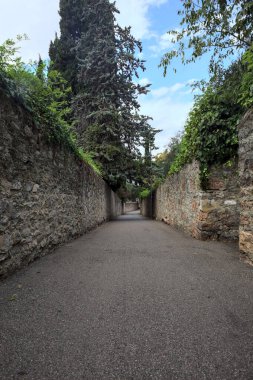 Bulutlu bir günde, İtalya 'nın bir köyünde ağaçlarla çevrili taştan duvarlarla çevrili taştan bir geçit.