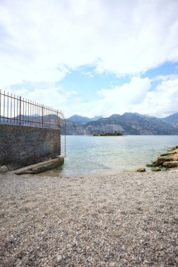 Kısmen bulutlu bir günde, dağlardaki bir gölün kıyısında çitle çevrili sınır duvarı.