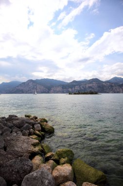 Kısmen bulutlu bir günde kıyıdan görünen bir dağ gölündeki küçük ada.