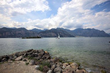 Kısmen bulutlu bir günde kıyıdan görünen bir dağ gölündeki küçük ada.