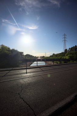 Gün batımında İtalya kırsalında ağaçlarla çevrili kontra ışıklandırılmış eğlence kanalı bir yol köprüsünden görülüyor.