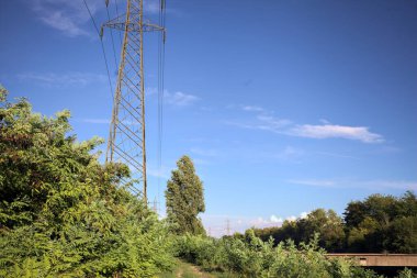 Yanı başında direği olan bitkilerle çevrili bir patika ve gün batımında İtalya 'nın kırsal kesimindeki bir eğlence kanalının kenarında bir elektrik hattı var.