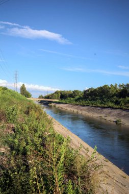 Bir patikanın yanında tarla sürmüş ve üzerinden elektrik hattı geçen saptırıcı bir kanal ve gün batımında İtalya kırsalında direği olan bir kanal.