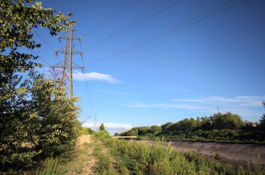 Yanı başında direği olan bitkilerle çevrili bir patika ve gün batımında İtalya 'nın kırsal kesimindeki bir eğlence kanalının kenarında bir elektrik hattı var.