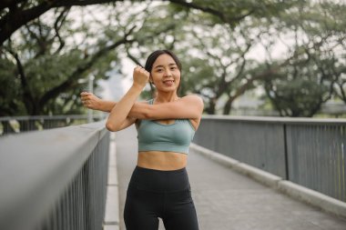 Asyalı mutlu kadın egzersizi, sabah parkta. Açık havada koşmadan önce spor giyinen ve esneyen sağlıklı bir kadın. Sağlık yaşam tarzı, dış faaliyetler.