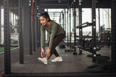 Formda spor salonunda egzersiz yapmadan önce vücut geren güçlü Asyalı kadın. Spor kıyafetleri giyen atlet kadın spor salonunda ağırlık ve halter gereçleriyle antrenman yapmadan önce.