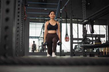 Güçlü Asyalı kadın spor salonunda kettlebell ile hamlesini yapıyor. Spor kıyafetleri giyen atlet kadın gri spor salonunda ağırlık ve halterli. Sağlıklı yaşam tarzı.