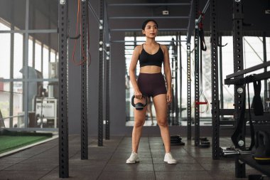 Güçlü Asyalı kadın spor salonunda kettlebell ile egzersiz yapıyor. Spor kıyafetleri giyen atlet kadın gri spor salonunda ağırlık ve halterli. Sağlıklı yaşam tarzı.