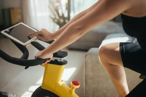 Asian woman exercising on stationary bike indoors at home. Healthy female training bike workout for cardio in living room. active and wellness lifestyle.