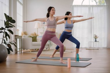 Spor giyimli iki Asyalı kadın ev stüdyosunda yoga yapıyor. Oturma odasında esneklik için yoga yapan birkaç kadın. Sağlık ve sağlık hizmetleri faaliyetleri.
