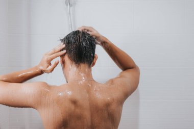 Adam saçlarını şampuanla yıkıyor ve banyoda duş alıyor, Asyalı erkek vücudu ve köpükle saç bakımı yapıyor. Spa ve Sağlık Hizmetleri.