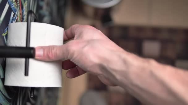 一个男人试图用手卷把卫生纸倒过来 他小心翼翼地打开厕纸 试图找出结局 行动发生在厕所里 — 图库视频影像