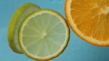 Turuncu ve kireç dilimleri su yüzeyinde hafifçe sallanıyor, narenciye dilimleri güzel bir şekilde süzülürken resim gibi bir manzara yaratıyor. Turuncu ve limon dilimlerinin sürüklenişini izleyin.