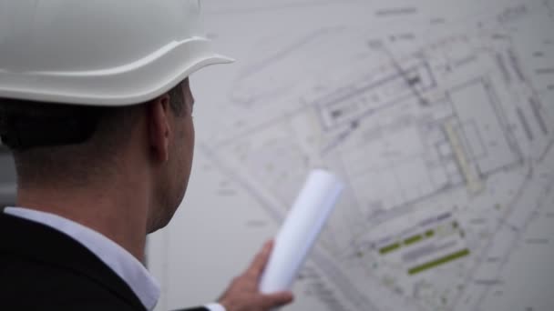 建筑师穿着商务服装 头戴白色头盔 分析项目图纸 建筑师指出细节 在建筑师手势语规划 建筑概念中准确地使用纸卷 — 图库视频影像