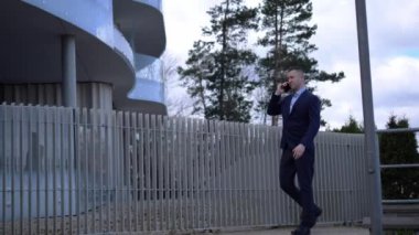 İş adamı kendinden emin adımlarla ilerler, telefonu kulağına bastırır. İş adamı pazarlık ederken, ofis binası arkasında beliriyor. İş adamının her adımı otoriteyi iletir ve odaklanır.