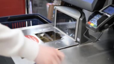 Riga, Letonya -28 Nisan 2024: Perakende satış ortamında, kadın self-servis istasyonunda ürün barkodunu tarıyor, zahmetsizce yönetiyor. Her taramada doğruluğu sağlamak için nesneleri hızlı bir şekilde tarar. Yazı