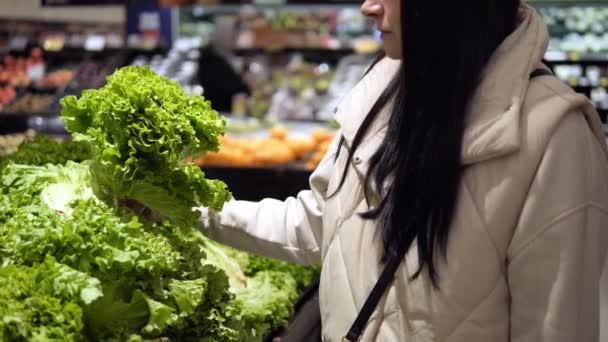 若いブルネットの女性は緑のサラダを調べ 緑のサラダの品質に焦点を当てたスーパーマーケットで慎重に緑のサラダを選択します 新鮮な食材と健康的なライフスタイルの選択肢を紹介するのに最適 — ストック動画