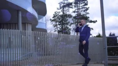 İş adamı, ofis inşaatının arka planına karşı telefonla kulaktan kulağa adımlar atıyor. İş adamı kritik anlaşmaları tartışıyor, odaklanmış ve iddialı. İşadamları onun profesyonel kararlılığını yansıtıyor.