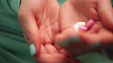 Bu videoda kadın eli, avuç içinden haplar alırken yakın plan çekiliyor. Giysilerin ve tırnakların yeşil rengi olay yerini vurguluyor, hapları alma ve tutma eylemine odaklanıyor.