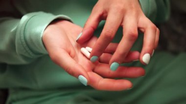 Bu görüntülerde kadın eli yakından çekilmiş, parmakları avuç içinden hap seçiyor. Giysilerin ve tırnakların yeşil rengi, haplarla etkileşime girerek görsel etkiyi arttırır..