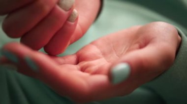 Yeşil tırnaklı ve elbiseli kadın elleri bir elden diğerine hapları atıyor ve sonra hapları yumruk hareketiyle örtüyor. Bu süreç boyunca hapların kontrol ve kontrol edilmesini vurguluyor..