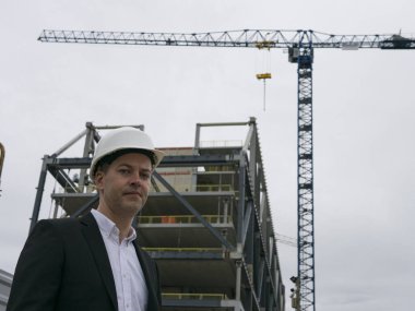 Beyaz kask takan, proje planını dikkatlice inceleyen genç erkek mimar konsantrasyonu, mimari hassasiyeti ve tasarım deneyimini gösteriyor..