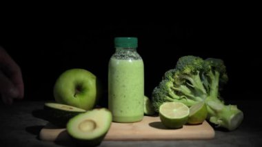 Şişe içinde taze yeşil smoothie, ahşap tahtadan meyve püresi toplamak. İçindekiler arasında avokado, limon, brokoli, salatalık arınma ve sağlığa odaklı içerik için birebir. Smoothie 'nin tadını çıkar
