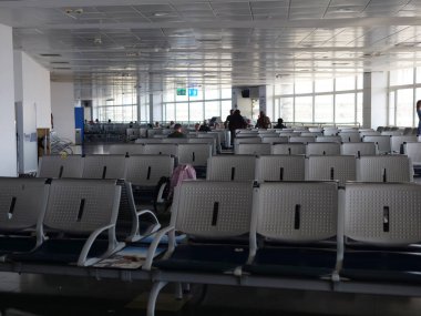 Havaalanında bekleme odasında, arkada sandalyeler ve insanlar var. Seyahat ve ulaşım için mükemmel. Havaalanı oturma alanı yolcularla dolu. Havaalanı terminalinin hareketli atmosferini yakala.