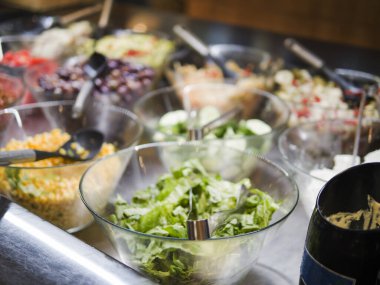 Cam salata kaselerinde metal kaşıkla çeşitli taze sebzeler rengarenk ve sağlıklı bir görüntü oluşturur. Taze sebzeler canlı besin ve tat sunar. Taze sebzeler servis edilmeye hazır..