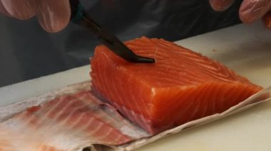 Eldivenli bir Japon aşçı taze somondan kemik çıkarmak için maşa kullanıyor. Becerikli hareketler somonların hassasiyetle hazırlanmasını sağlar. Kemikleri çıkarmak somonu pişirmeye hazır hale getirir..