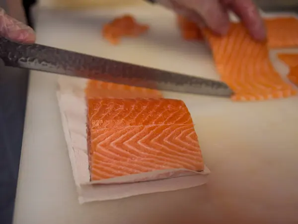 stock image Fresh salmon is sliced into even portions by a master of Japanese cuisine. Each stroke of the knife reveals the rich color and tender texture of the salmon, reflecting the chefs expertise.