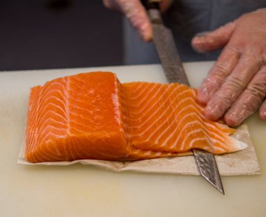 Şefi, hassasiyet ve zarafetle taze somonu parçalara ayırır. Keskin bıçak, somon balığının içinde zahmetsizce süzülür. Her kesik somon balığının hazırlanmasındaki kalite ve özeni gözler önüne serer..