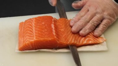 Taze somon Japon mutfağının ustası tarafından dilimlenir. Bıçağın her vuruşu somon balığının zengin rengini ve yumuşak dokusunu gözler önüne seriyor, şefin uzmanlığını yansıtıyor..