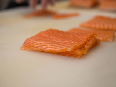 El değmemiş bir somon balığı dikkatlice mutfak tahtasına konur ve ince tabakaları ışığın altında parlar. Somonların canlı renkleri tazeliğini ve kalitesini vurgular..