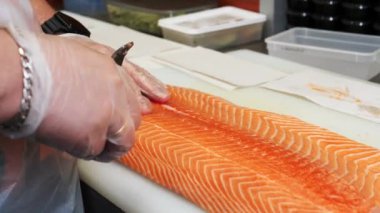 Eldivenli bir Japon aşçı, maşalı büyük bir somondan kemikleri dikkatlice çıkarıyor. Kullanılan hassasiyet somonun mükemmel bir şekilde hazırlanmasını sağlar. Somonu pişirmeye hazır hale getirmek için her adım hayati önem taşıyor..