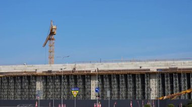 İşçiler inşaat binasında ilerliyorlar, dikkatle ilerliyorlar ve vinç yukarıda yükseliyor. Bu inşaat sahnesi beton bina üzerinde yürürken ilerlemeyi gösteriyor..