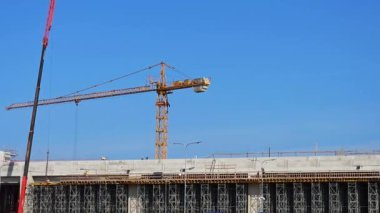 İşçilerin beton bölümlerde yürüdüğü, günlük ilerleme gösteren yoğun bir inşaat binası. Arka planda dik duran bir vinç, bu inşaat binasının gücünü ve büyümesini simgeliyor..