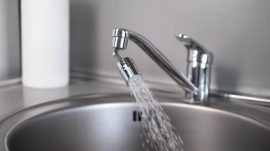Su sürekli olarak metal bir musluktan lavaboya akar ve yumuşak bir akış oluşturur. Musluklar ışık altında parıldar damlacıklar etrafa sıçrarken, işleyen bir musluğun özünü yakalar..