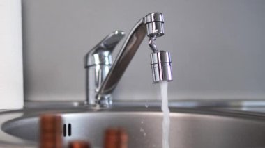 Madeni paralar, bir musluktan akan su gibi organize sütunlar halinde dimdik dururlar. Musluklar metalik paralarla tezat oluşturuyor, çarpıcı bir görsel hareketle hareket ve dinginliği harmanlıyor..