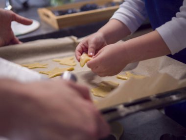 Çocuk sıcak mutfakta kurabiye hamuru şekillendiriyor, festival sezonunda ailesi tarafından çevrelenmiş. Kurabiye hamuru ile ilgili beceriler geliştirirken değerli anılar yaratmak neşe getirir. 