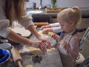 Anne ve kızları sıcak bir mutfakta yıldız şeklinde kurabiyeler yapıyorlar, pişirme üzerine kaynaşıyorlar. Neşeli aile anları samimi bir görüntüyle çekildi: Yemek pişirme, tatiller, aile işleri, neşe, ilham
