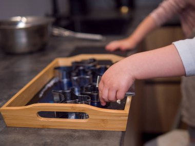 Küçük çocuk, modern bir mutfakta çeşitli şekilli kurabiye kesicileri hamur haline getirerek her kurabiyeyi özenle canlandırıyor. Her kesik çocuğun kurabiye şeklini öğrenmesine ve zevk almasına yardımcı olur.. 