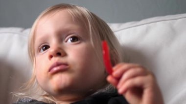 Sarışın genç çocuk beyaz koltukta dinleniyor, kırmızı biberin tadını çıkarıyor ve komik yüz ifadelerini paylaşıyor. Genç çocuk bu neşeli anda masumiyet ve haz saçıyor.. 