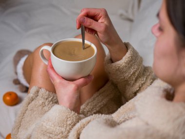 Bej bornozlu genç bir kadın evinde rahatça oturup, metal kaşıkla bir fincan kahve karıştırıyor. Etrafı mandalinalarla çevriliyken, sabahları kahvesini yudumlarken kahvaltıda dinleniyor.